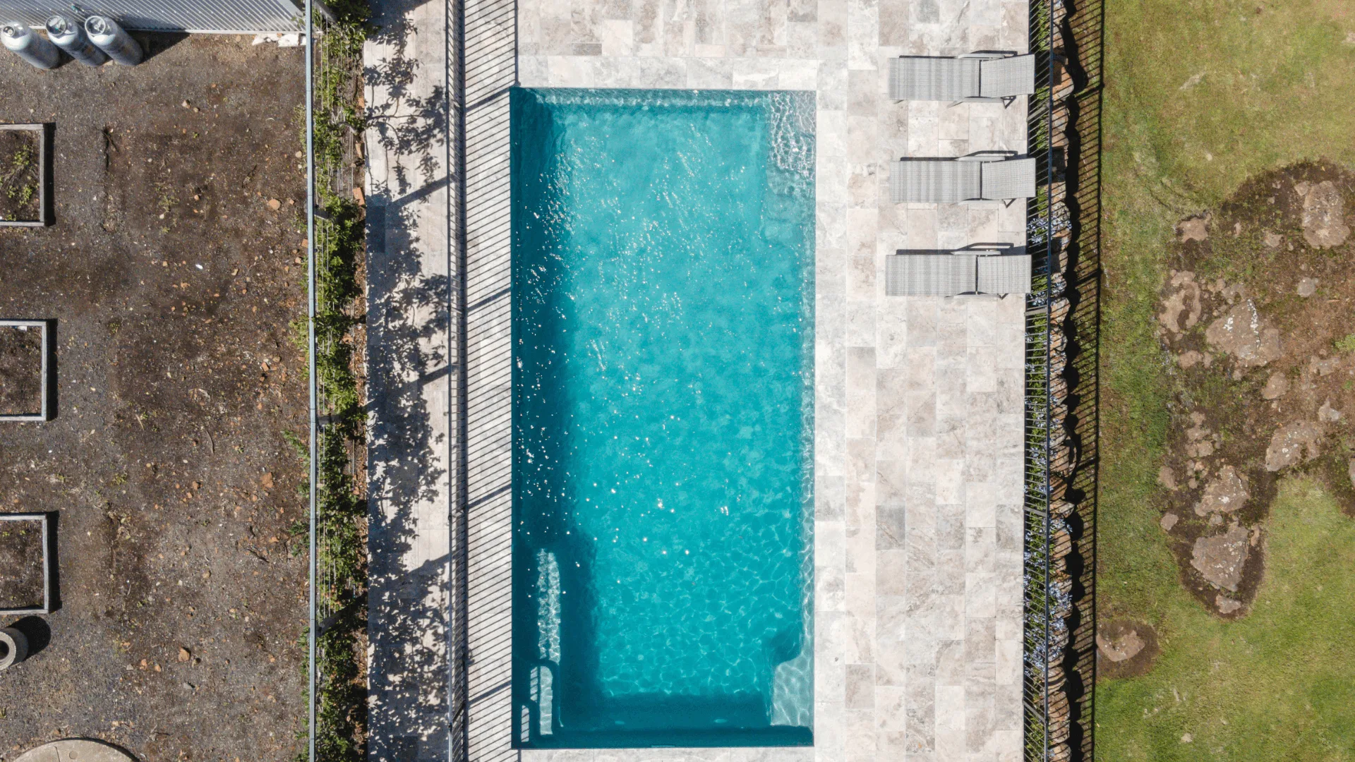 aerial view of a rectangular fiberglass swimming pool with clear blue water surrounded by a stone patio and lounge chairs